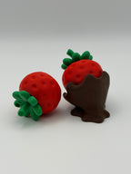 Two red strawberry fidget clickers with green leaves in a chocolate covered base.