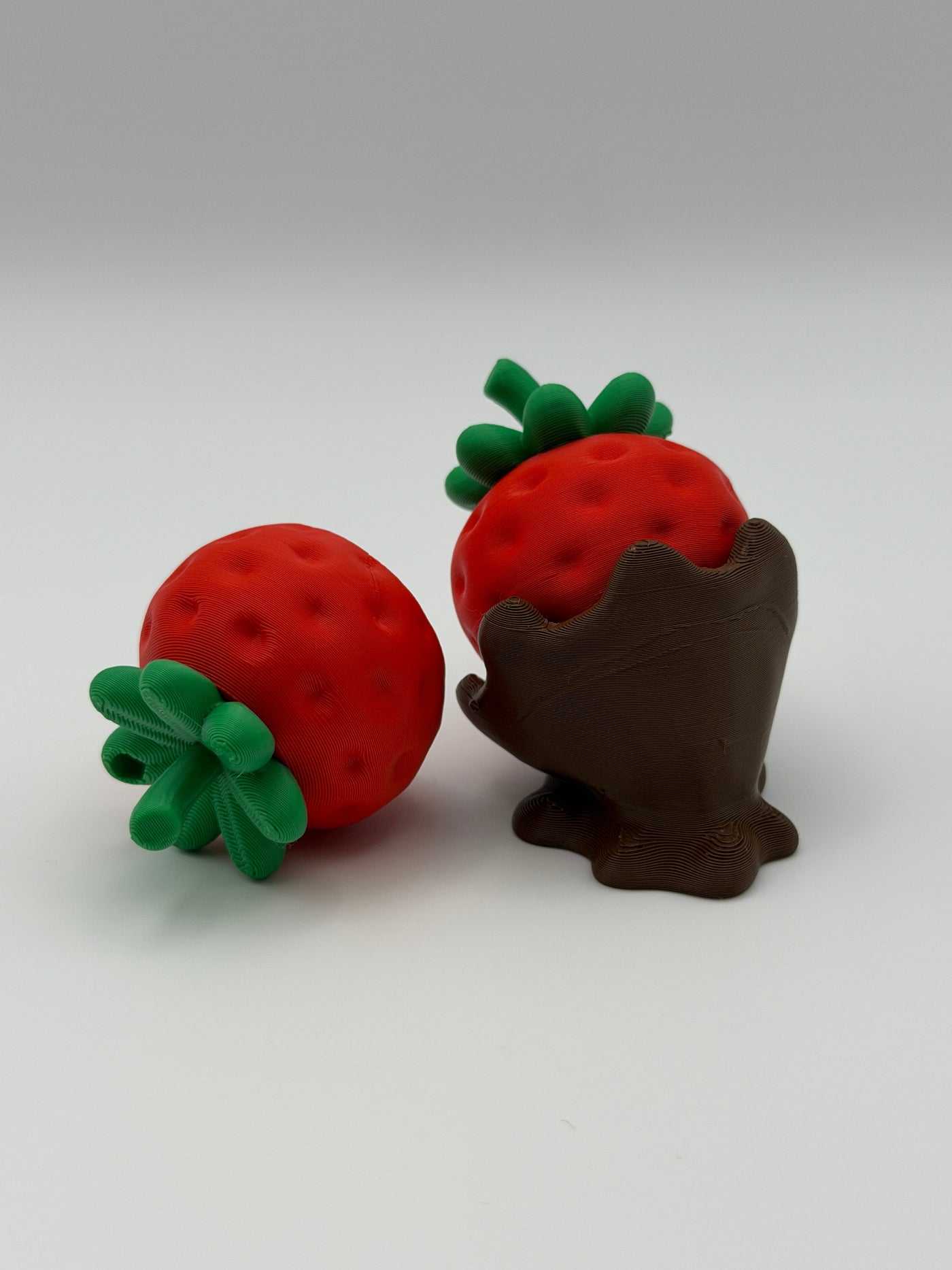 Two red strawberry fidget clickers with green leaves in a chocolate covered base.