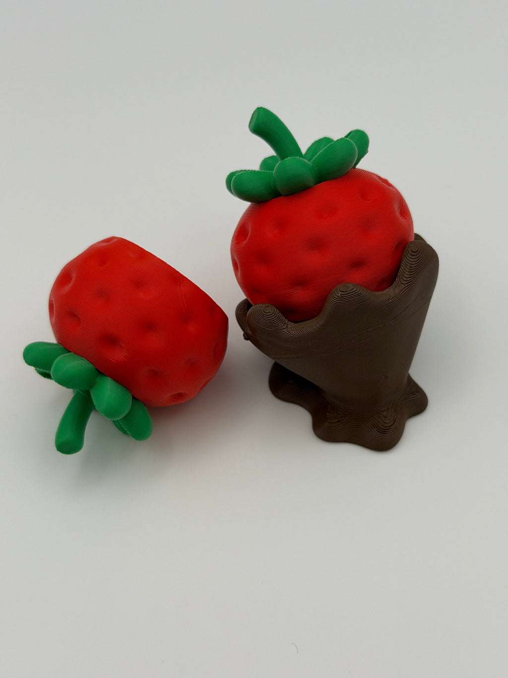 Two red strawberry fidget clickers with green leaves in a chocolate covered base.