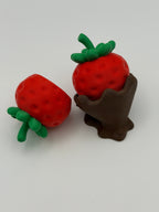 Two red strawberry fidget clickers with green leaves in a chocolate covered base.
