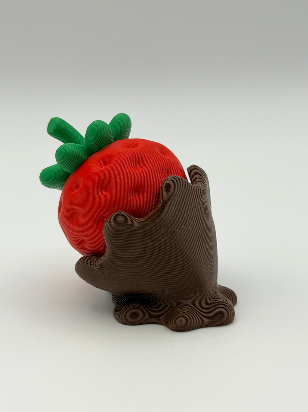 A red strawberry fidget clicker with green leaves in a chocolate covered base.