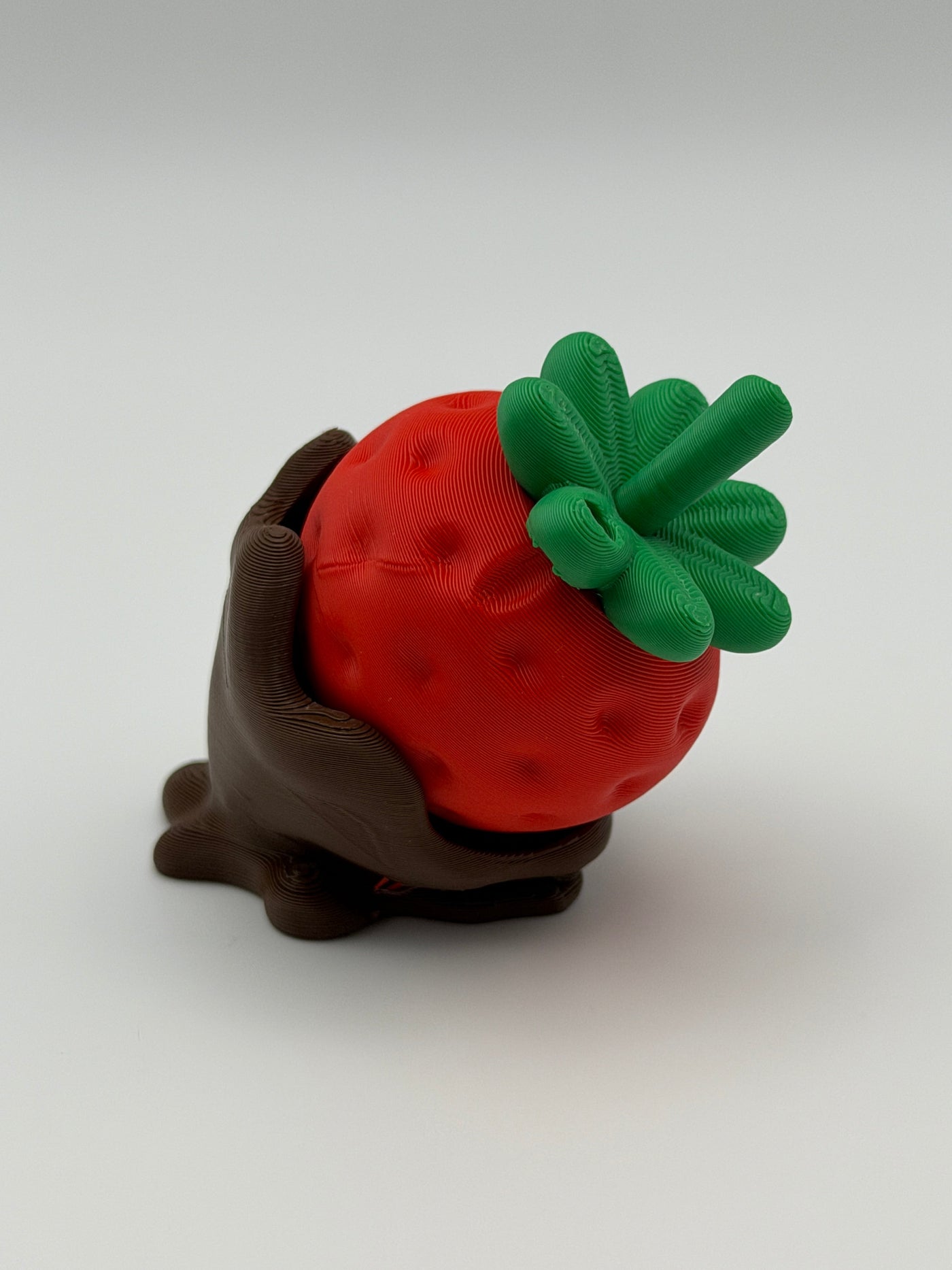 A red strawberry fidget clicker with green leaves in a chocolate covered base.