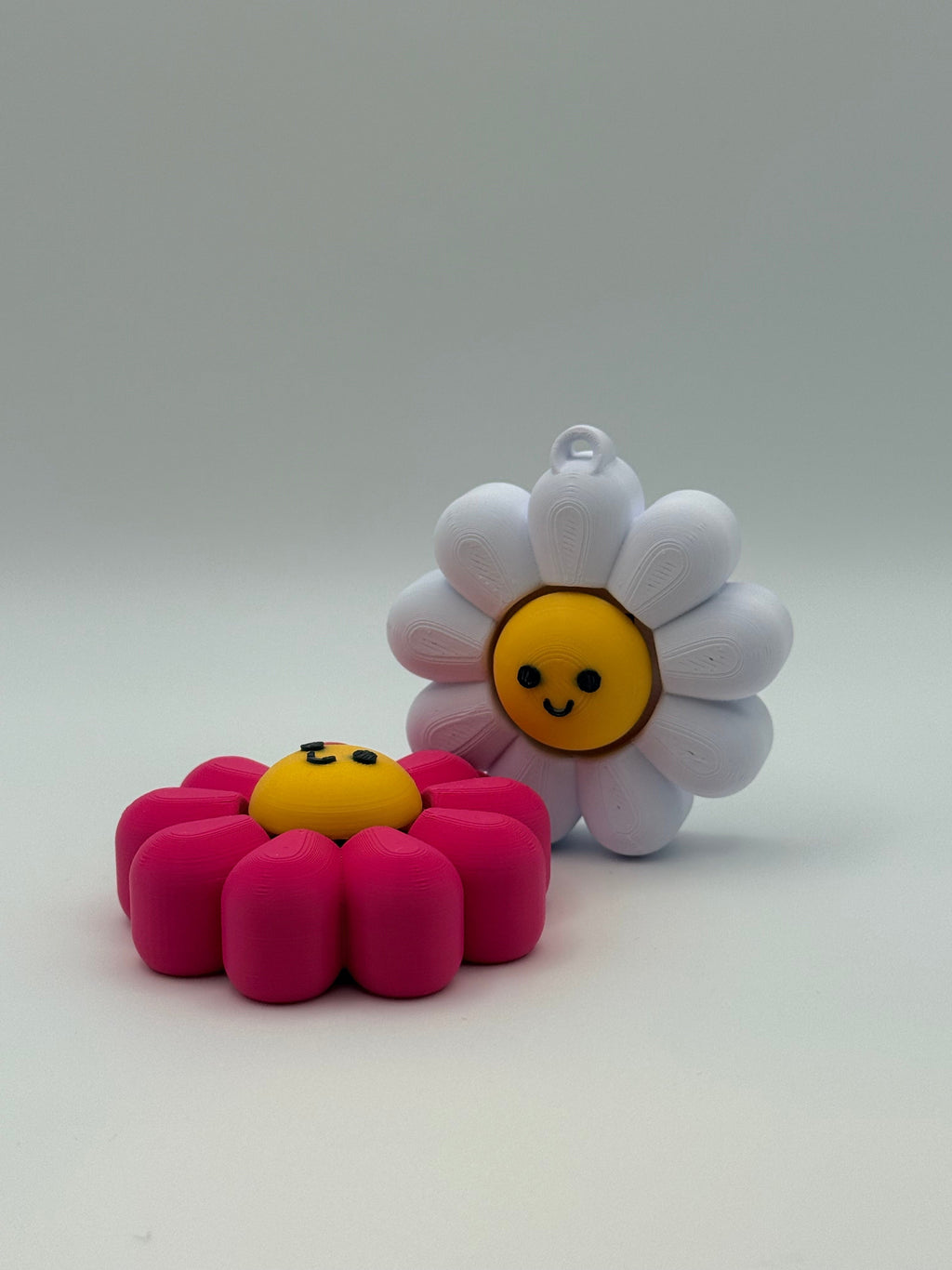 Two Daisy fidget clickers with yellow centers and a black smiley face. Pink and yellow individual clickers.