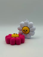 Two Daisy fidget clickers with yellow centers and a black smiley face. Pink and yellow individual clickers.