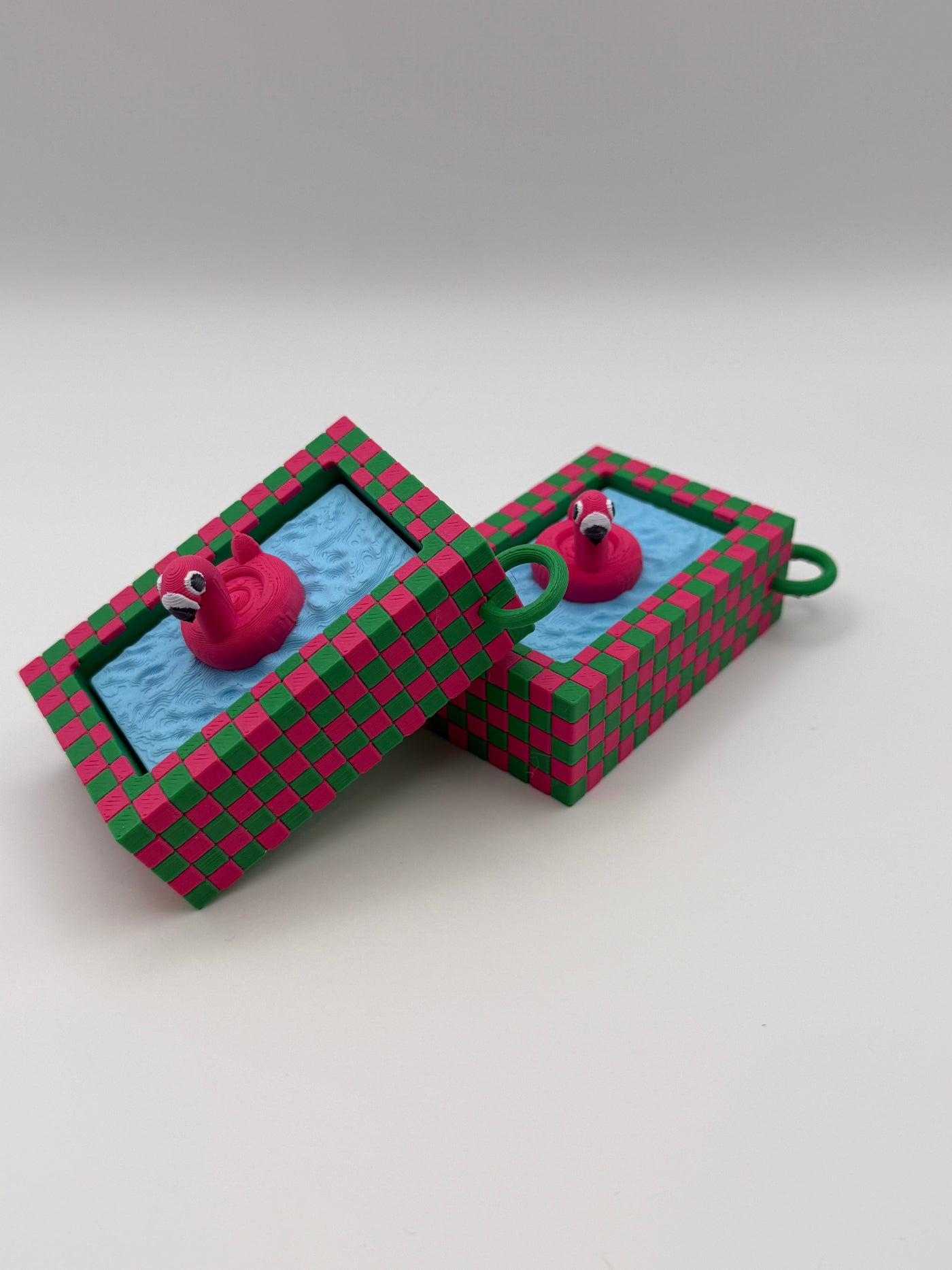 Two pink flamingo in a blue pool fidget clickers with a green keychain and textured pink and green external base.