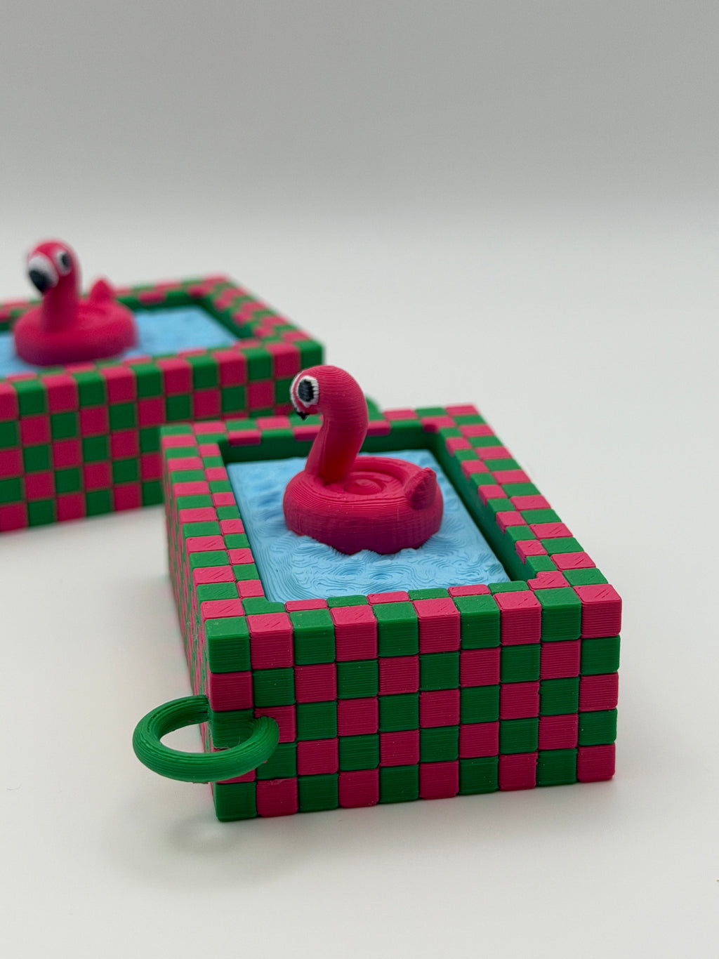 Two pink flamingo in a blue pool fidget clickers with a green keychain and textured pink and green external base.