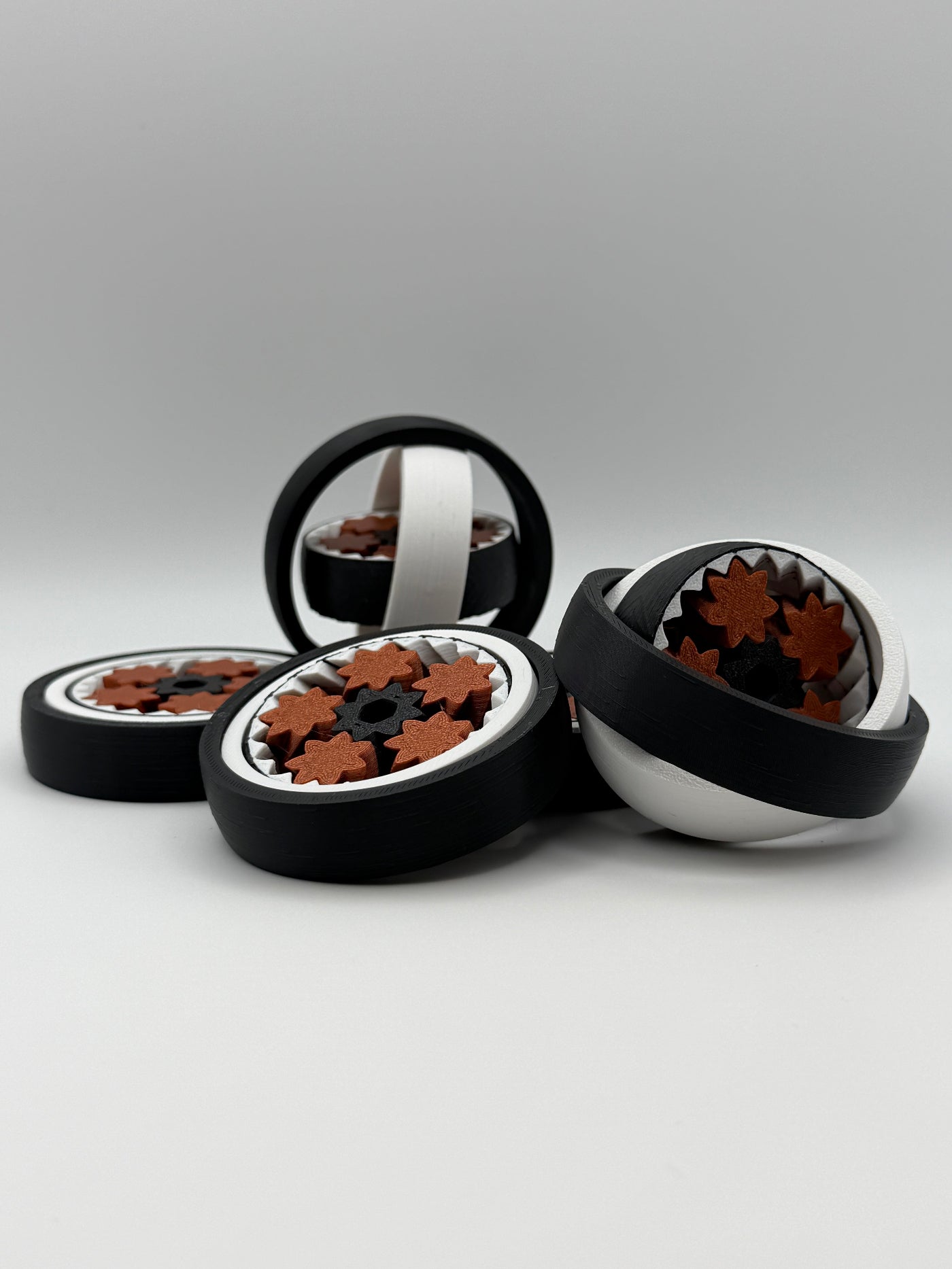Four gyro spinning fidget toys. A black exterior layer, followed by a white layer, followed by another black layer that spins. 5 bronze coloured star shape wheels wrapped around a black star shape cog that spins the bronze wheels. 