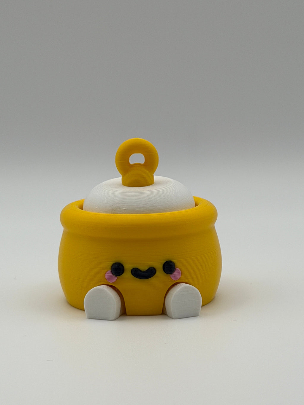 A yellow honey pot with a white fidget clicker top and a yellow keychain attachment with white articulated legs and a black smiley face. 
