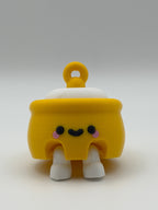 A yellow honey pot with a white fidget clicker top and a yellow keychain attachment with white articulated legs and a black smiley face. 