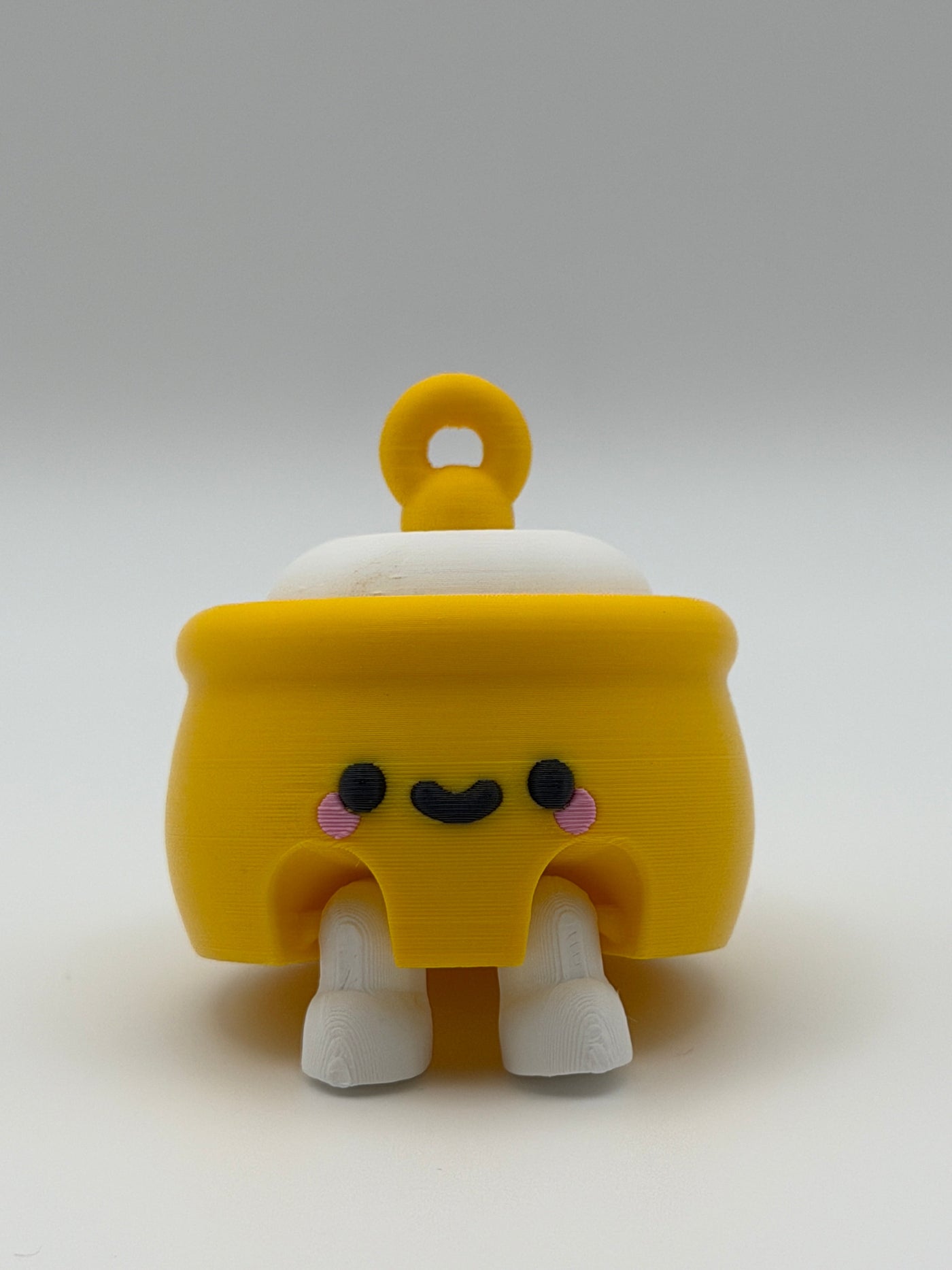 A yellow honey pot with a white fidget clicker top and a yellow keychain attachment with white articulated legs and a black smiley face. 