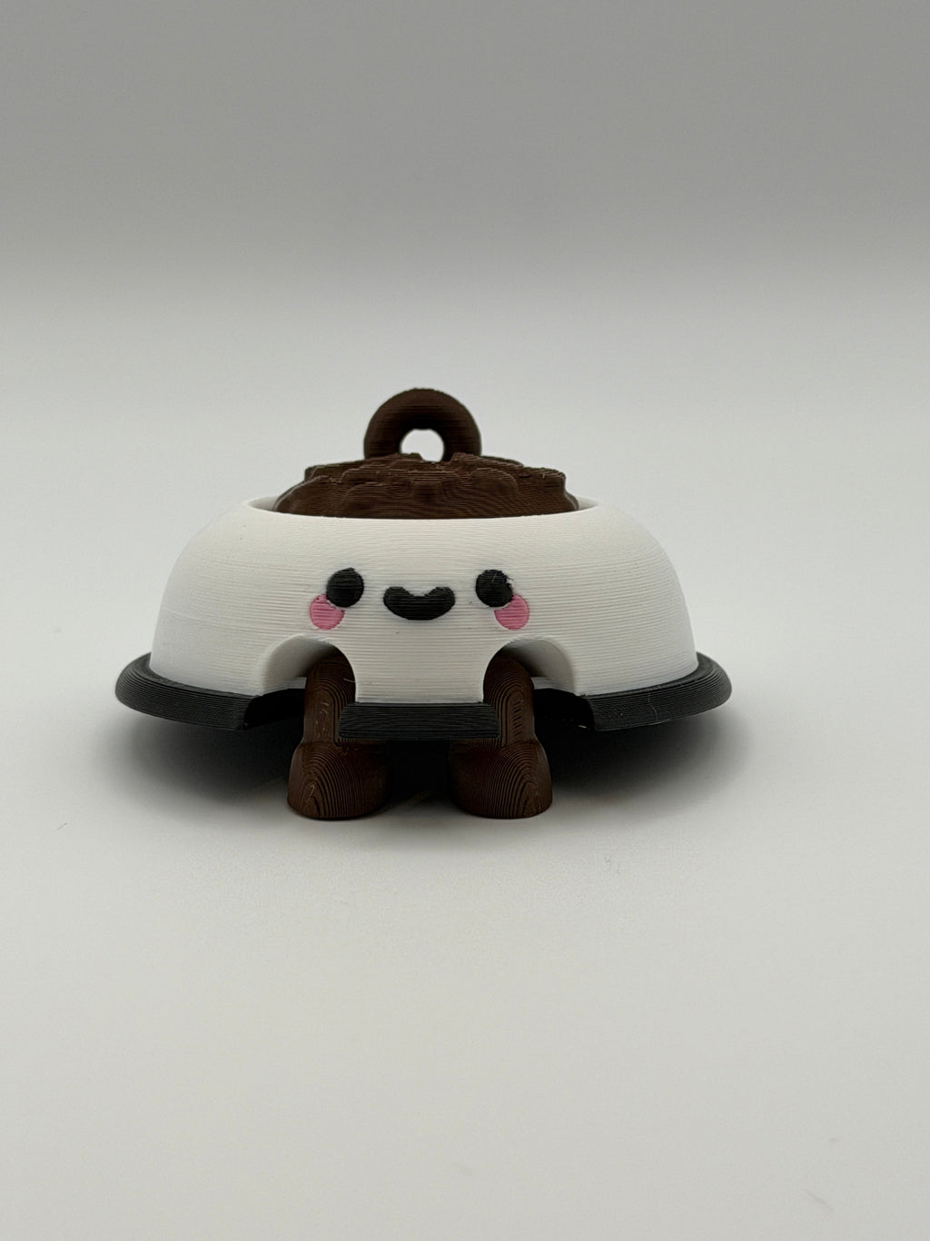 A white dog bowl with brown food and a keychain attachment. The white bowl has a black smiley face and the legs are brown and articulated. 