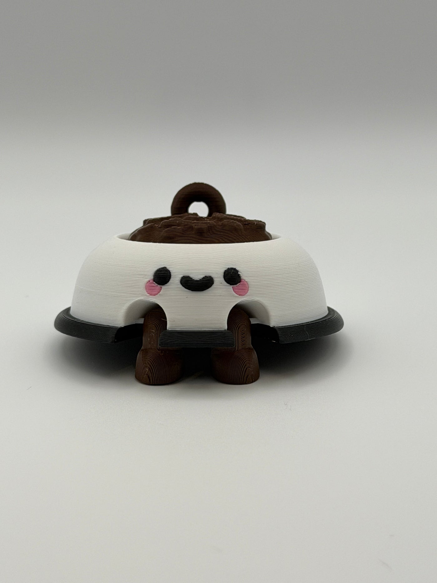 A white dog bowl with brown food and a keychain attachment. The white bowl has a black smiley face and the legs are brown and articulated. 