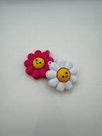 Two Daisy fidget clickers with yellow centers and a black smiley face. Pink and yellow individual clickers.
