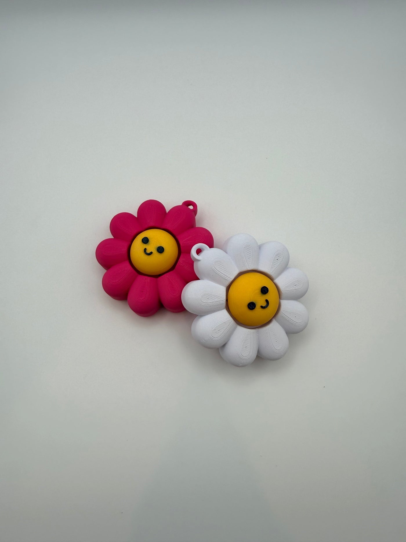 Two Daisy fidget clickers with yellow centers and a black smiley face. Pink and yellow individual clickers.