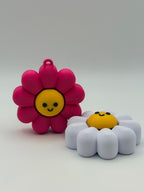 Two Daisy fidget clickers with yellow centers and a black smiley face. Pink and yellow individual clickers.