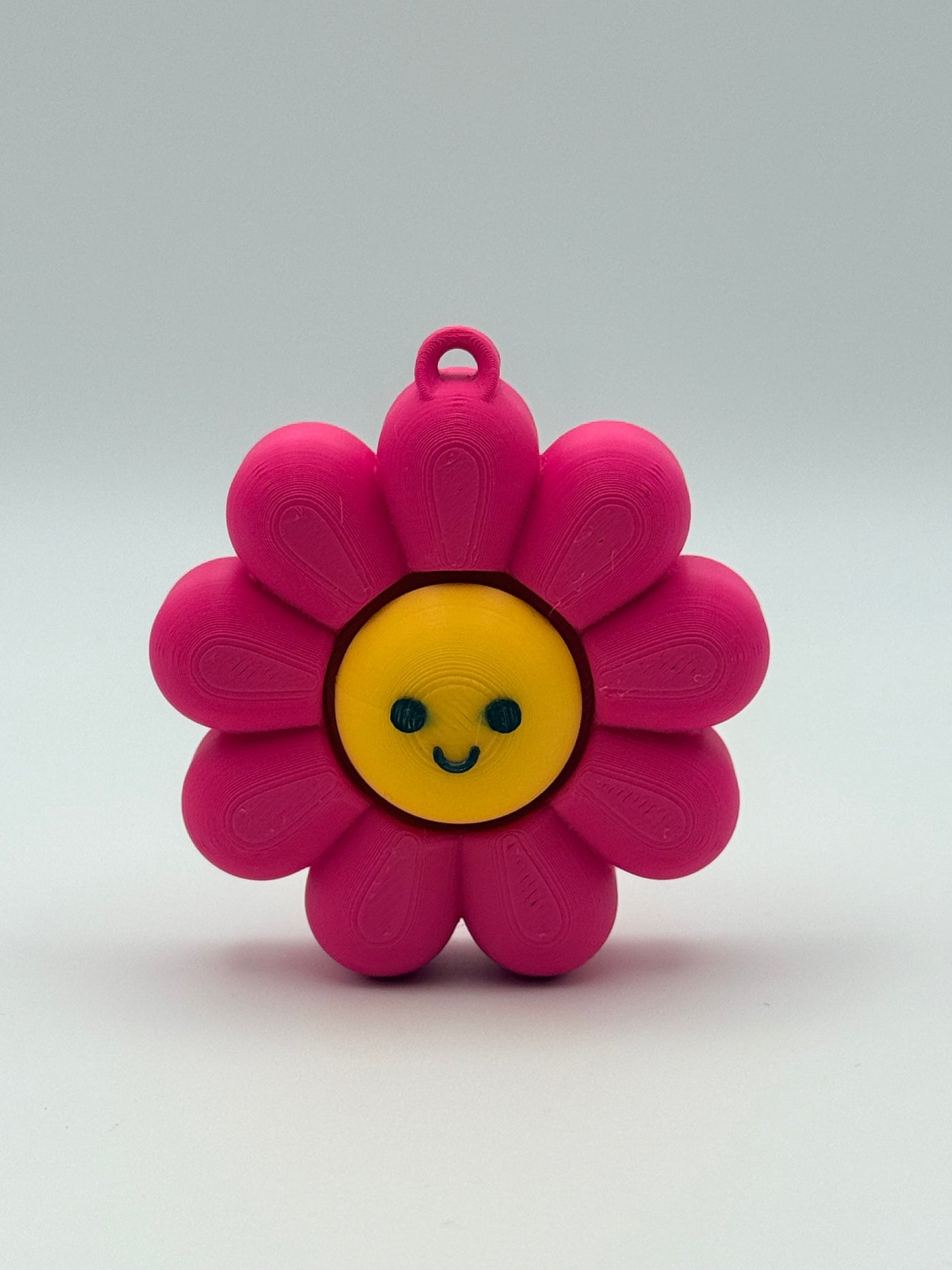 Pink flower-shaped object with a black smiley face and yellow center on a white background