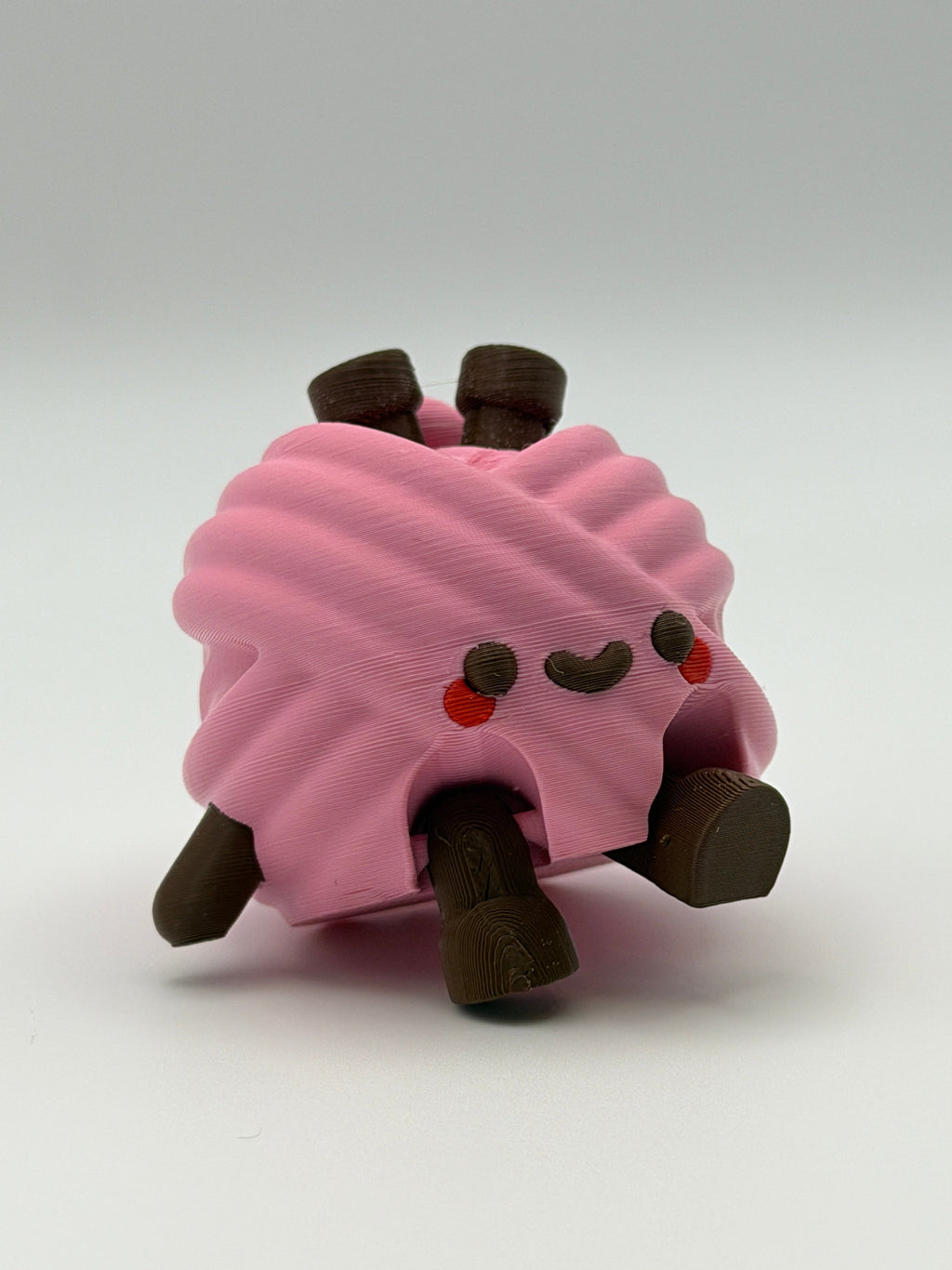 A pink articulated yarn ball fidget clicker with brown feet, one brown hand, and two brown needles in the head.