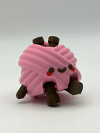 A pink articulated yarn ball fidget clicker with brown feet, one brown hand, and two brown needles in the head.