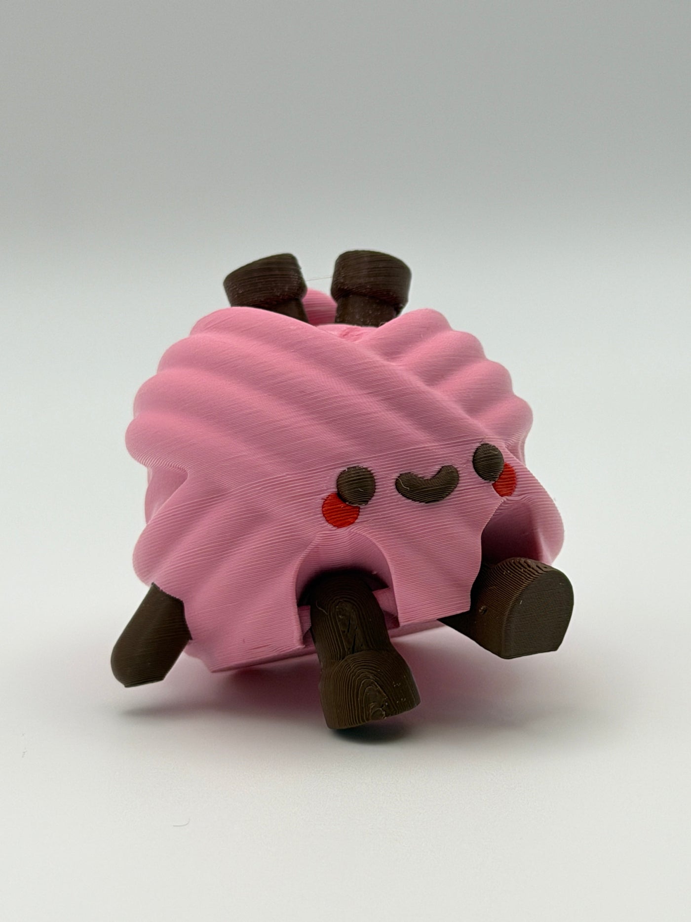 A pink articulated yarn ball fidget clicker with brown feet, one brown hand, and two brown needles in the head.