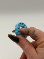 Hand holding a blue plastic ring with star patterns on a plain background