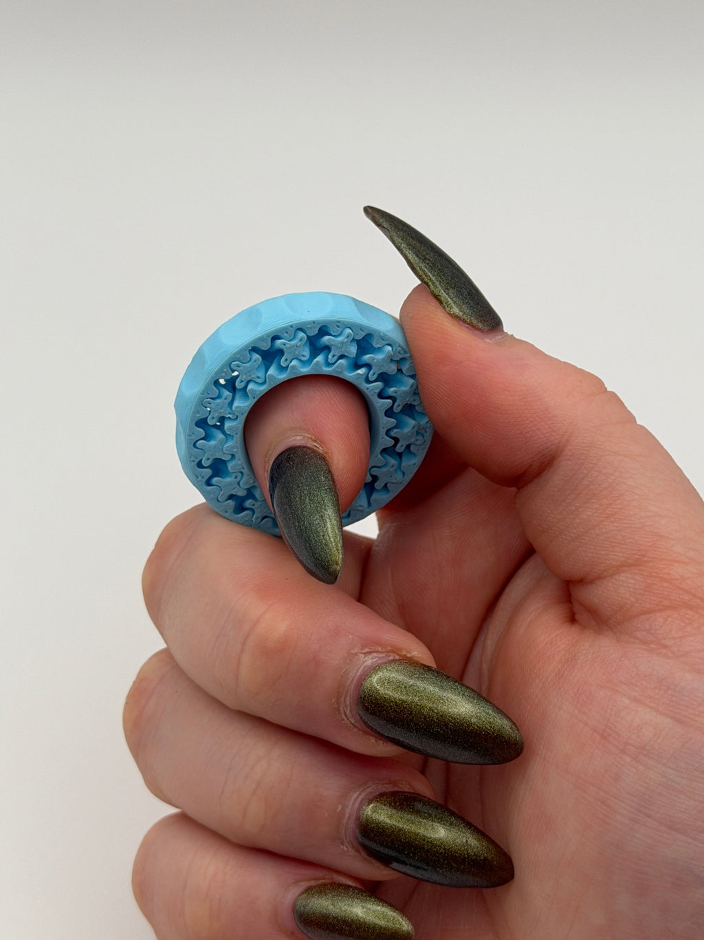 Hand with green nail polish holding a blue textured object against a white background