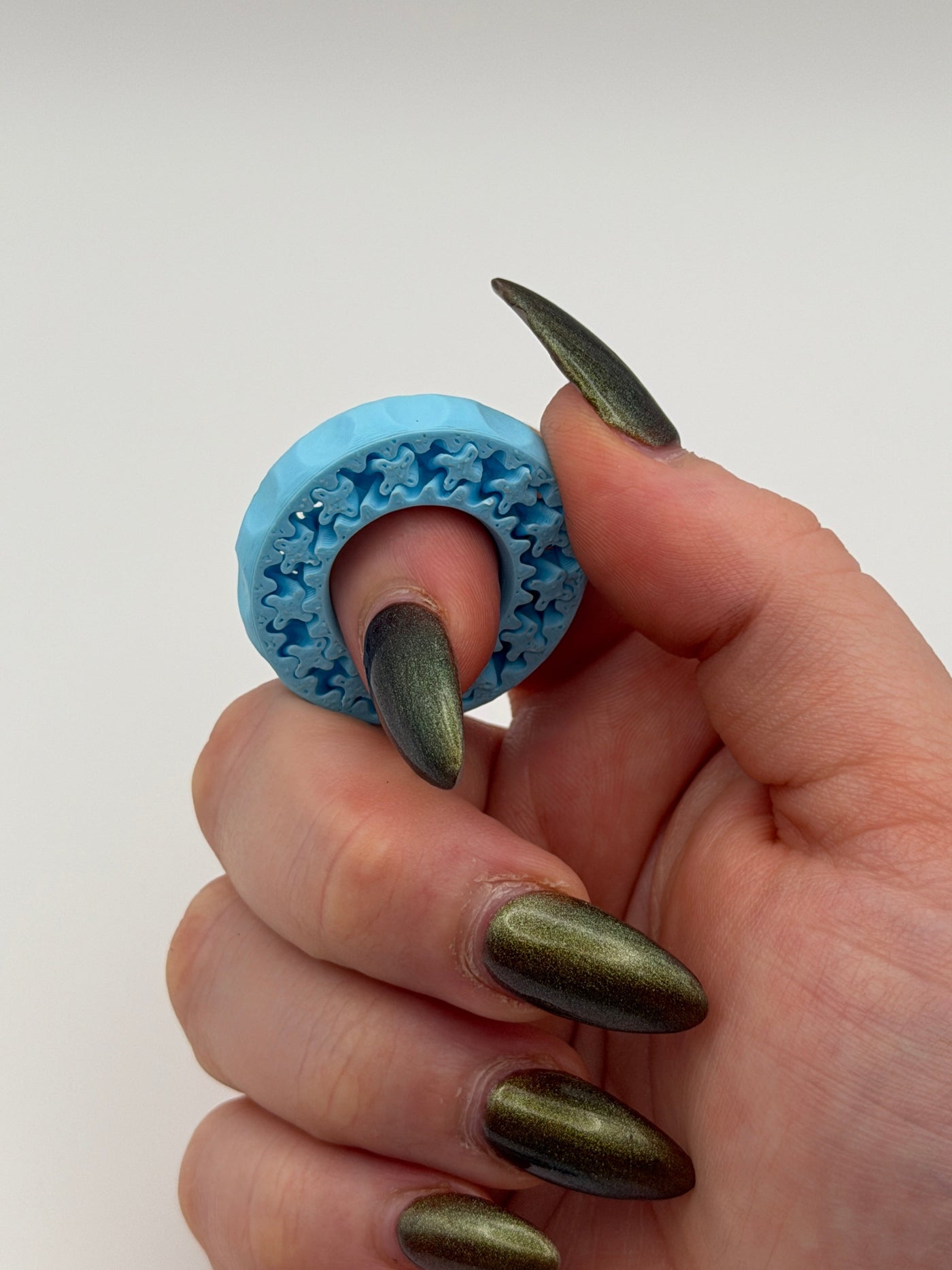 Hand with green nail polish holding a blue textured object against a white background