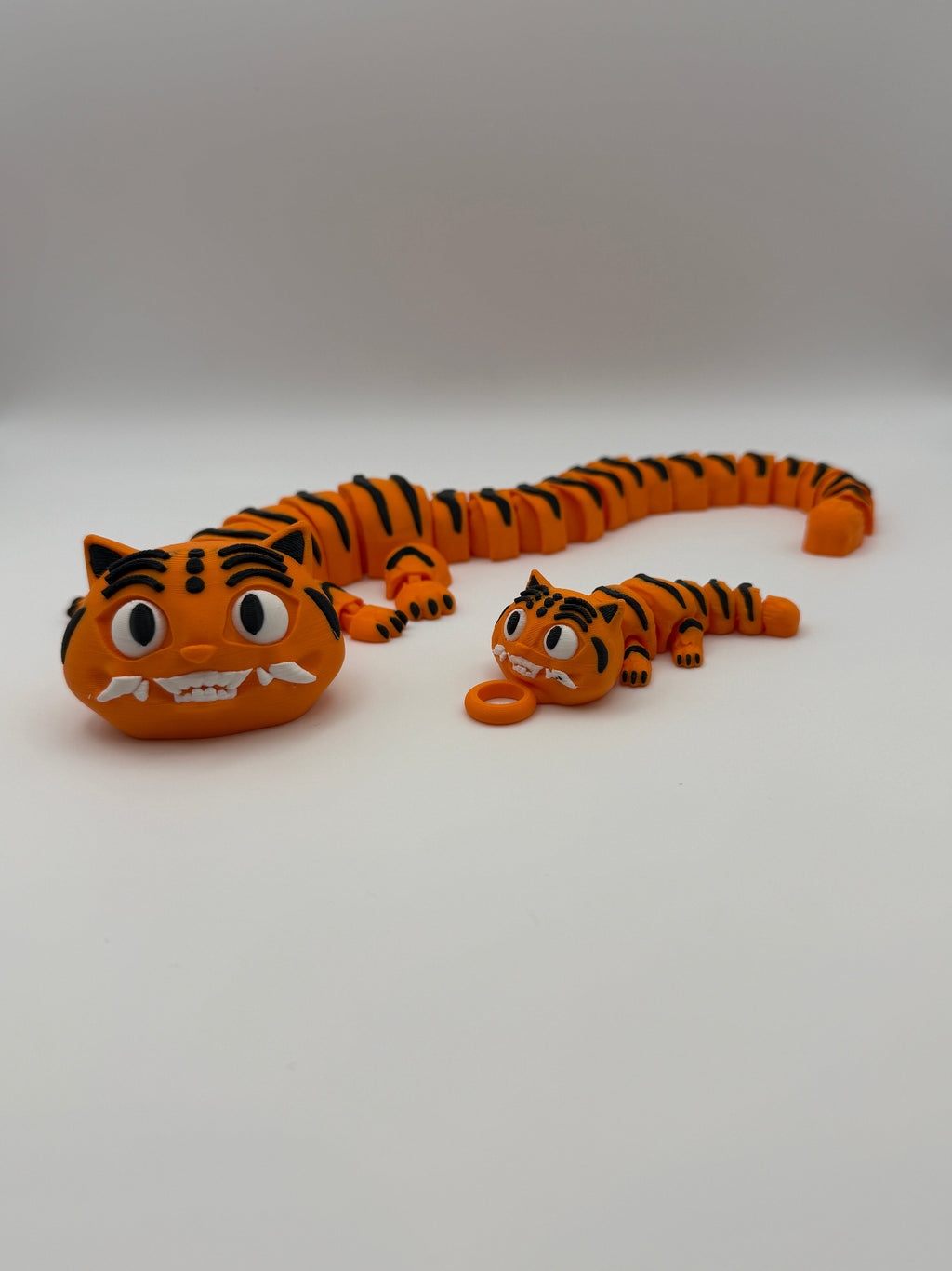 Two large and small articulated orange tigers with black stripes and grinning teeth.  The small one has a keychain attachment. 