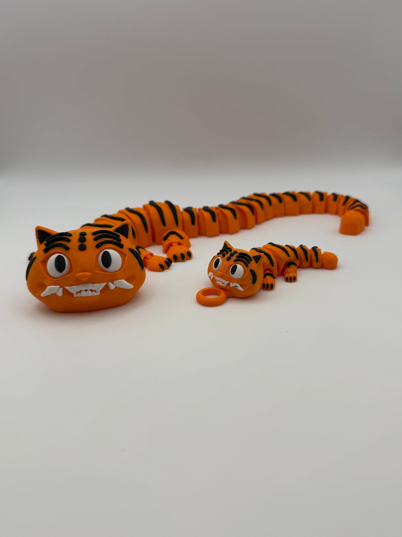 Two large and small articulated orange tigers with black stripes and grinning teeth.  The small one has a keychain attachment. 