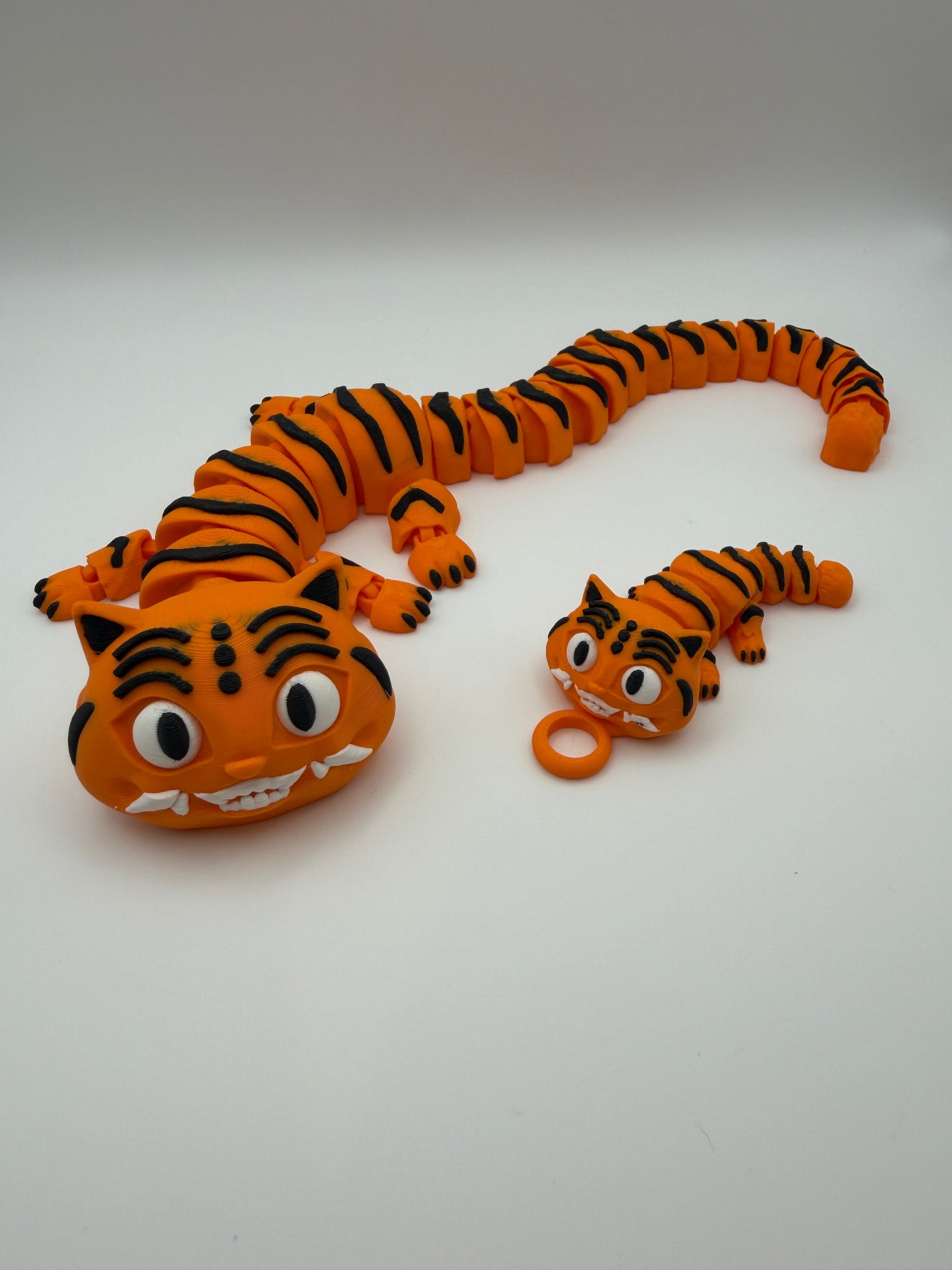 Two orange and black striped tiger articulated toys with grinning teeth. One is large,  the other is small with a keychain attachment. 