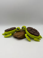 Two green and brown shelled fidget clicker turtles on a rock base. 