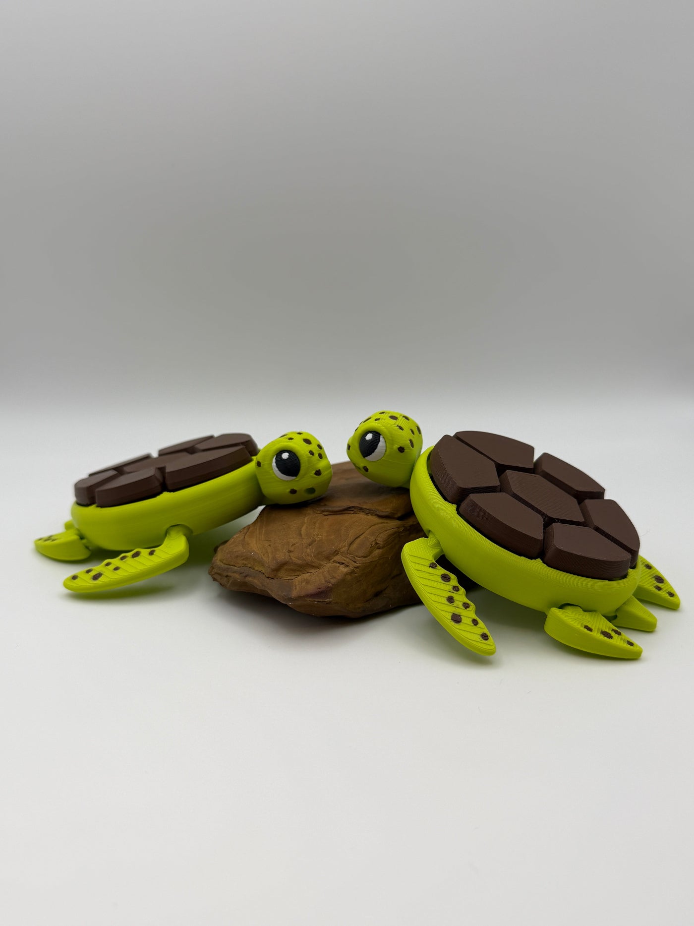 Two green and brown shelled fidget clicker turtles on a rock base. 