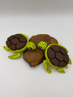 Two green and brown shelled fidget clicker turtles on a rock base. 