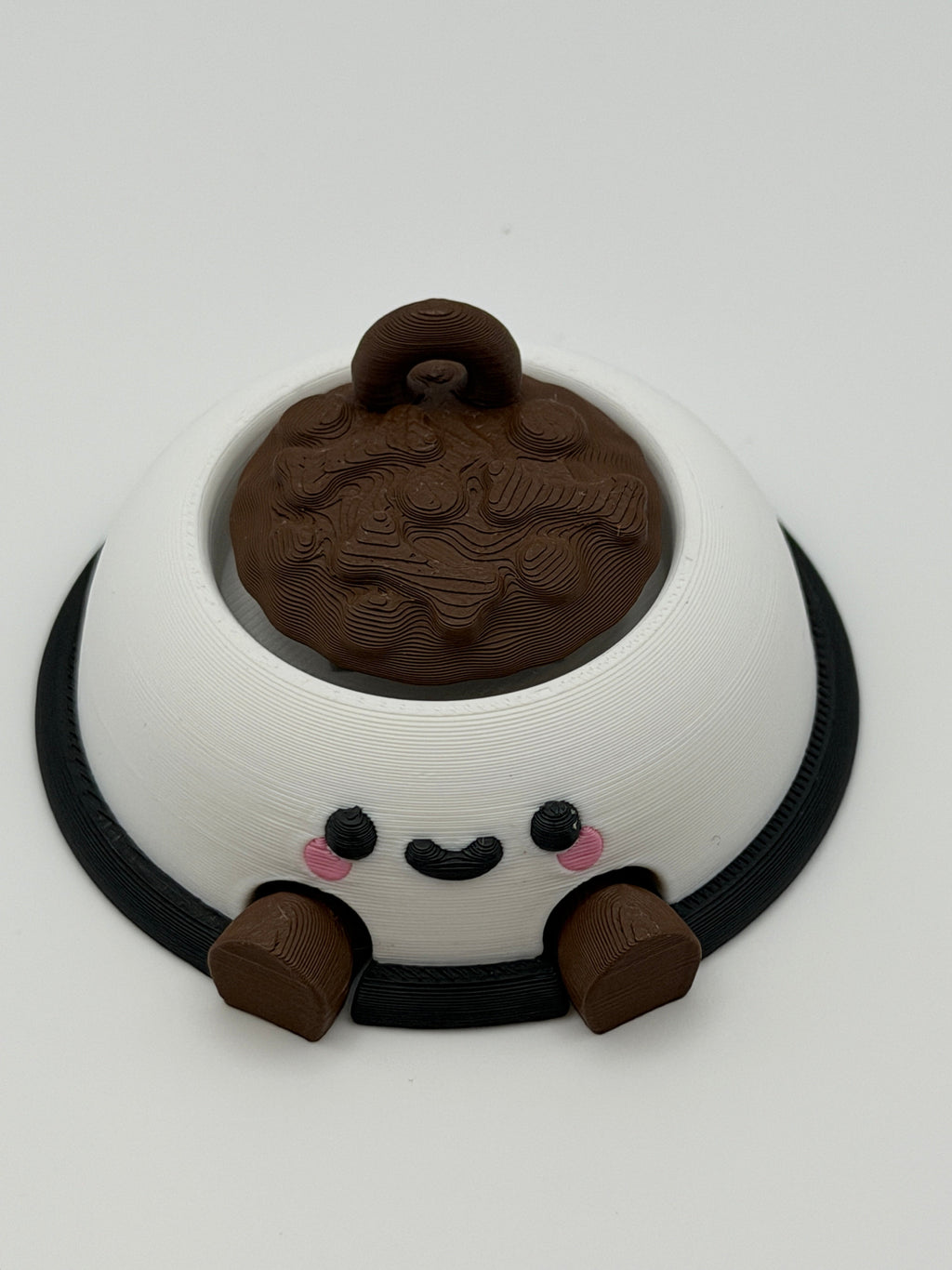 A white dog bowl with brown food and a keychain attachment. The white bowl has a black smiley face and the legs are brown and articulated. 