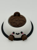 A white dog bowl with brown food and a keychain attachment. The white bowl has a black smiley face and the legs are brown and articulated. 