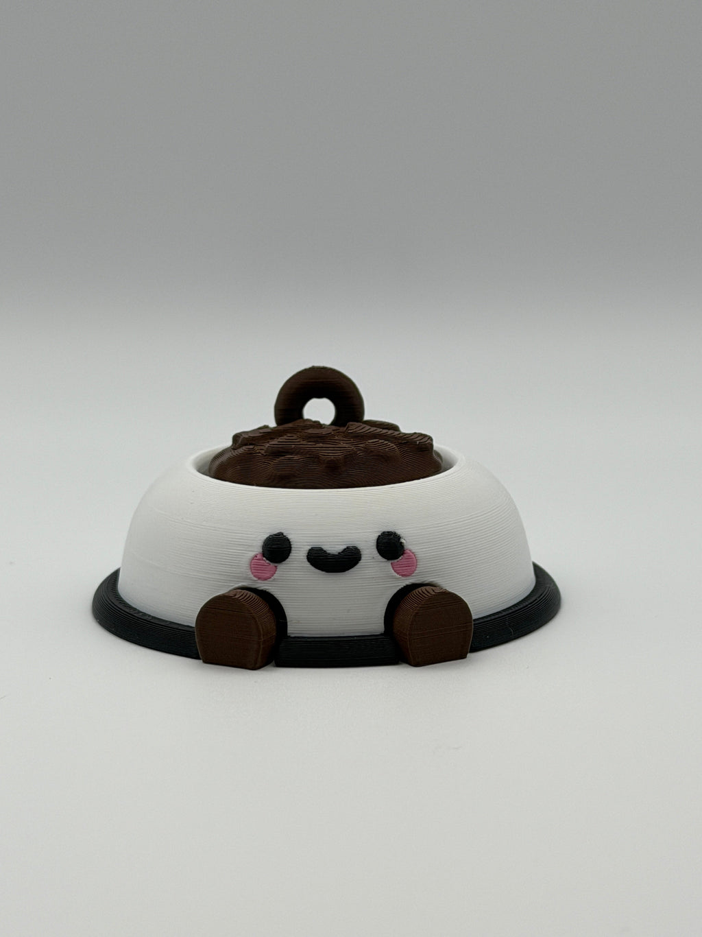 A white dog bowl with brown food and a keychain attachment. The white bowl has a black smiley face and the legs are brown and articulated. 