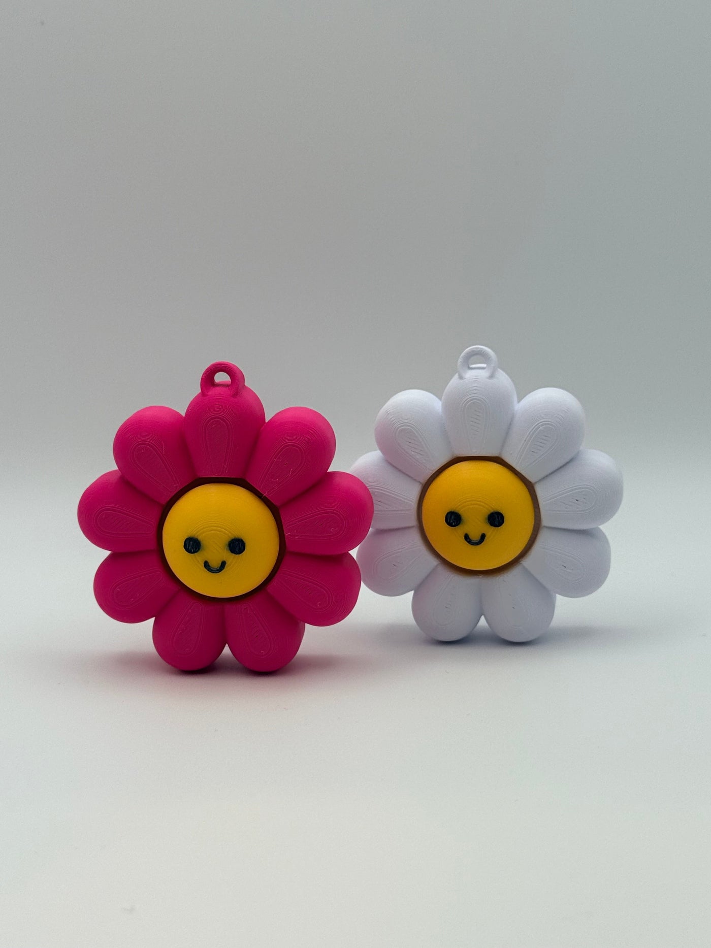 Two Daisy fidget clickers with yellow centers and a black smiley face. Pink and yellow individual clickers.