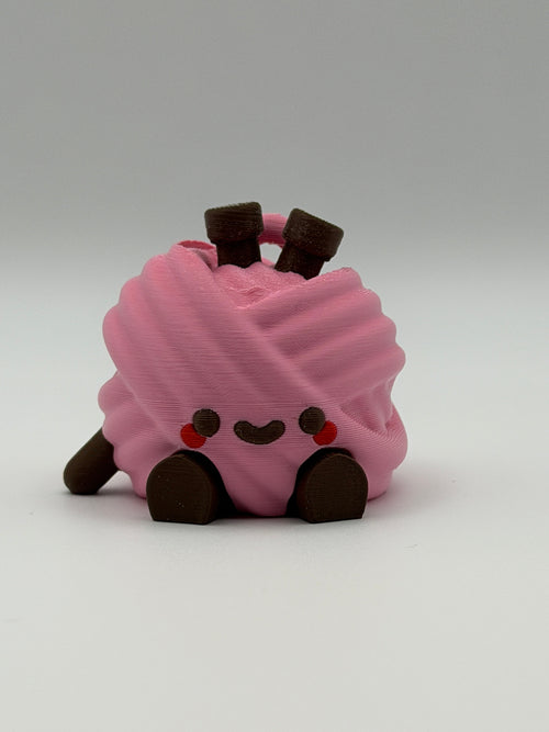 A pink articulated yarn ball fidget clicker with brown feet, one brown hand, and two brown needles in the head.